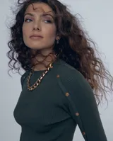 Polera gris de tejido de punto con cuello redondo y mangas largas. Presenta detalle de botones metálicos en los hombros y puños.