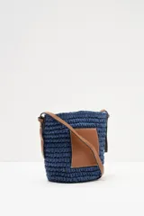 Bolso bandolera azul tejido con bolsillo de cuero marrón en el frente y correa larga de cuero marrón.