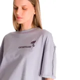Remera gris de corte amplio con mangas cortas y ruedo recto. Presenta un pequeño estampado con el logo de Caterpillar y una flor en el lado izquierdo del pecho.