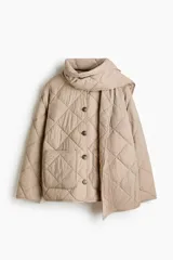 Campera acolchada de color beige con diseño guateado en rombos, hombros caídos, cuello redondo, cierre frontal de botones y bolsillos parche delanteros. Incluye una bufanda a juego que se abrocha en la nuca y cuenta con aislamiento térmico THERMOLITE.