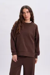 Sudadera de cuello redondo y manga larga en color marrón, con diseño holgado y detalle de etiqueta en la manga.
