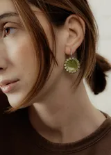 Aros colgantes con forma circular, hechos de resina color lila y borde de strass plateado. El aro es de acero quirúrgico plateado.