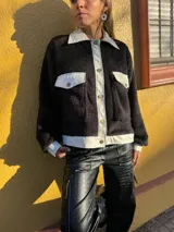 Campera de corderito negra con cuello, solapa, puños y bolsillos de cuero sintético color crema.