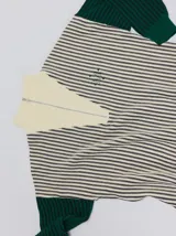 Pullover de tejido acanalado grueso con cuello alto y cierre frontal parcial. Presenta un diseño de bloques de color, con cuerpo en tono beige y mangas en contraste con rayas verticales en tonos rojizos. Incluye un detalle bordado en el pecho.