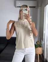 Blusa blanca sin mangas, de símil lino, con cuello alto y detalle de encaje calado y volados en el escote.