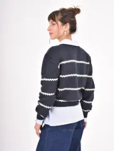 Buzo de tejido de punto en color azul marino con rayas horizontales blancas en diseño de zigzag. Presenta cuello redondo, mangas largas y puños acanalados.