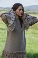 Sweater de lana merino color beige, con silueta amplia y relajada. Presenta mangas largas con volumen, terminaciones con volados de lino y flecos en los puños y en el ruedo, además de detalles trenzados a lo largo de las mangas.