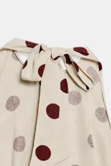 Top beige con estampado de lunares bordó, cuello halter, diseño sin mangas y bajo con volantes. Cuenta con cierre de lazada en la espalda.