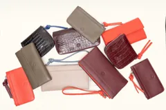 Billetera rectangular de cuero con textura de reptil, cierre perimetral y correa de muñeca lateral. Presenta un pequeño aplique metálico circular en el centro.
