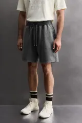 Short tipo jogger de algodón con interior afelpado, cintura elástica ajustable con cordón, bolsillos frontales y bolsillo trasero. Presenta un efecto lavado y estampado gráfico a contraste en el frente.