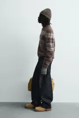 Jersey de punto con textura, corte relajado, cuello redondo y manga larga. Presenta un diseño jacquard geométrico con motivos de copos de nieve en tonos marrones, azules y blancos.