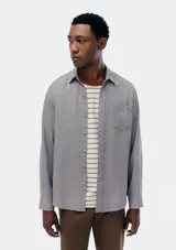 Camisa de manga larga en color gris, con cuello clásico, cierre frontal de botones y un bolsillo en el pecho.