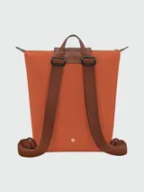 Mochila Longchamp modelo Le Pliage Original en tamaño M, color rosado con solapa y detalles en cuero marrón. Cuenta con correas ajustables de tela y cierre superior con solapa de botón a presión.