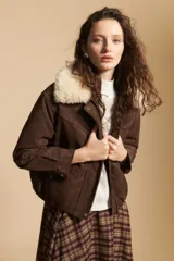 Campera de gamuza color marrón con cuello de corderito sintético en color crema. Presenta cierre frontal, bolsillos laterales con broches metálicos y puños rectos.