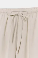 Pantalón palazzo de tiro alto, color beige claro, confeccionado en lino 100%. Presenta cintura ajustable con cordones anudados al frente y pierna ancha.