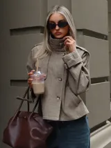 Chaqueta corta de estilo trench con estampado de cuadros pequeños, cuello alto, cierre frontal de doble botonadura y mangas con trabillas ajustables en los puños.