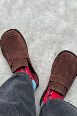 Mocasines de gamuza color marrón con costuras pespunteadas en color rojo y detalle de tira en el empeine.