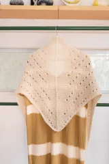 Chal triangular tejido a mano en lana de alpaca natural color crudo, con diseño calado y terminación con borlas.