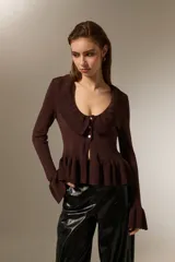 Top de punto color marrón, con cuello redondo amplio, cierre frontal con botones, mangas largas con puños acampanados y detalle de volados en el cuello y el ruedo.