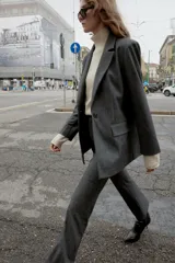 Blazer recta gris con hombreras, cuello solapa, manga larga, bolsillos delanteros con solapa y cierre frontal con un botón.