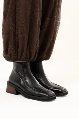 Bota de cuero color chocolate con horma cuadrada, taco bloque de madera y plataforma. Presenta cierre lateral interno y detalle de ribete en la capellada.