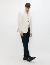 Blazer de medio forro color beige, confeccionado en mezcla de algodón y lino. Presenta una silueta estructurada con solapas de muesca, cierre frontal de un botón y bolsillos con solapa.