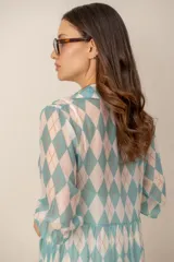 Vestido midi turquesa y blanco con estampado de rombos, cuello camisero, cierre frontal con botones y mangas cortas abullonadas. Cuenta con recortes fruncidos en la falda.