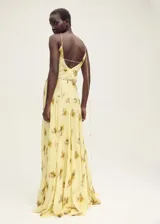 Vestido largo de tirantes finos con cuello de pico, confeccionado en viscosa con estampado floral difuminado en tonos amarillos y marrones. Presenta un diseño recto con detalle de cadena metálica a la altura de la cadera y cierre de lazo en la espalda.
