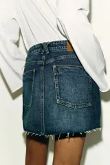 Falda pantalón de denim azul con diseño de cinco bolsillos, cierre frontal con cremallera y botón, y bajo deshilachado sin costuras.