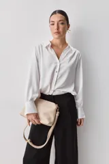 Camisa blanca de manga larga con textura suave y caída liviana, cuello camisero, puños anchos y fruncidos sutiles en los hombros.