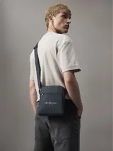 Bandolera Calvin Klein Jeans gris con logo estampado en el frente, bolsillo externo con cierre y correa ajustable.