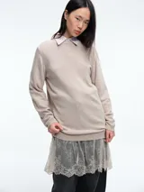 Sweater de tejido de punto color beige, con cuello redondo y mangas largas. Presenta un diseño de largo extendido con un delicado aplique de encaje en el ruedo inferior.