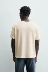 Camiseta de manga corta y cuello redondo, color azul marino, con ribete de contraste en color crema alrededor del cuello.