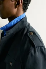 Chaqueta estilo militar relaxed fit de color azul marino, confeccionada en mezcla de algodón y lino. Presenta cuello subido, manga larga con puño abotonado, hombros con trabillas y cuatro bolsillos delanteros de parche con solapa. Se cierra al frente con botonadura metálica dorada.