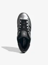 Championes Adidas Superstar con acabado metalizado plateado, caracterizadas por su icónica puntera de goma y las tres bandas laterales en color negro. Presentan una suela de plataforma negra y detalles en contraste en el talón y la lengüeta.