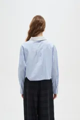 Camisa de algodón a rayas verticales en tonos celestes y blancos, con cuello camisero en contraste color blanco, manga larga y corte cropped.