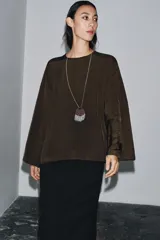 Blusa de cuello redondo y manga larga, confeccionada en tejido fluido con acabado satinado. Presenta un diseño de corte holgado, bajo recto y cierre en la espalda mediante una pequeña abertura con botón.