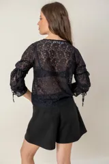 Blusa de encaje negro con escote en V, mangas tres cuartos y detalle de fruncido central con cordón ajustable.