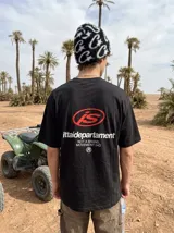 Remera negra de manga corta y corte oversize, con estampa en la espalda que incluye el logo 'IS' en rojo y texto blanco con la leyenda 'ittaidepartament NOT A BRAND, MOVEMENT 04D'.