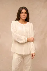 Camisa de algodón color crudo, con mangas largas abullonadas y puños elásticos. Presenta diseño con bordados tipo broderie en toda la prenda y cierre frontal con botones.