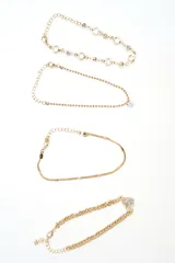 Set de cuatro pulseras doradas de diferentes diseños: una con cristales incrustados, una fina con dijes colgantes, una de cadena tipo víbora y una de cadena gruesa con un dije de corazón pavé.