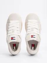 Zapatillas Tommy Jeans de corte bajo, color gris claro, confeccionadas en ante con interior de poliéster y suela de goma color caramelo. Presentan cordones blancos, logo de la marca en la lengüeta y etiqueta de Tommy Jeans en el lateral.