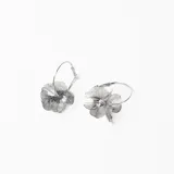 Aros tipo argolla con dije de flor metálica calada en color plateado.