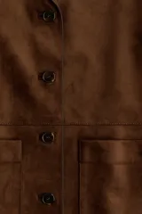 Campera marrón de tejido suave con acabado cepillado, solapas de muesca, cierre frontal de botones oscuros y bolsillos frontales tipo parche. Cuenta con forrería interior.