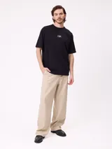 Remera negra de corte holgado con pequeño logo bordado en el pecho que incluye un diseño de pez y la marca Rusty.