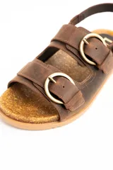 Sandalia de cuero marrón con dos tiras con hebillas metálicas en el empeine y tira ajustable en el talón. Cuenta con base anatómica de corcho y suela dentada.