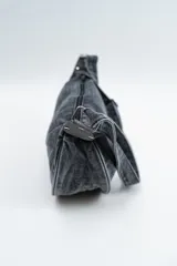 Cartera tipo bandolera de denim color negro, con diseño de media luna y correa ajustable.