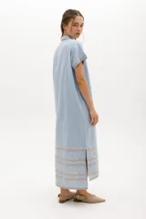 Vestido camisero de lino color lila con bordados rojos en contraste. Presenta un diseño de largo midi con cuello camisero, cierre frontal de botones y mangas cortas. Los detalles bordados recorren la botonadura, los puños y el ruedo de la prenda.