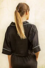 Bolero corto negro con estampado labrado, cuello tipo camisa, manga corta, cierre frontal con botones dorados y ribete blanco en cuello, mangas y ruedo.
