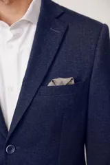 Blazer de corte slim fit en color marrón con textura jaspeada, cierre frontal de dos botones, solapas clásicas y bolsillo en el pecho con pañuelo decorativo.